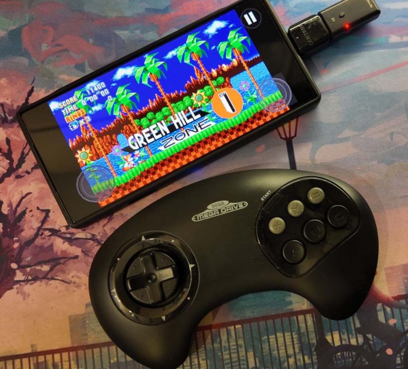 retro-bit sega mega drive controller with sonic mania plus on a phone in the background
